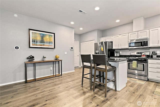 kitchen with a breakfast bar, light wood finished floors, visible vents, appliances with stainless steel finishes, and white cabinetry