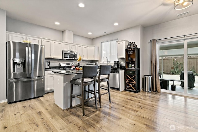 kitchen featuring stainless steel appliances, a kitchen island, white cabinets, light wood-type flooring, and dark countertops