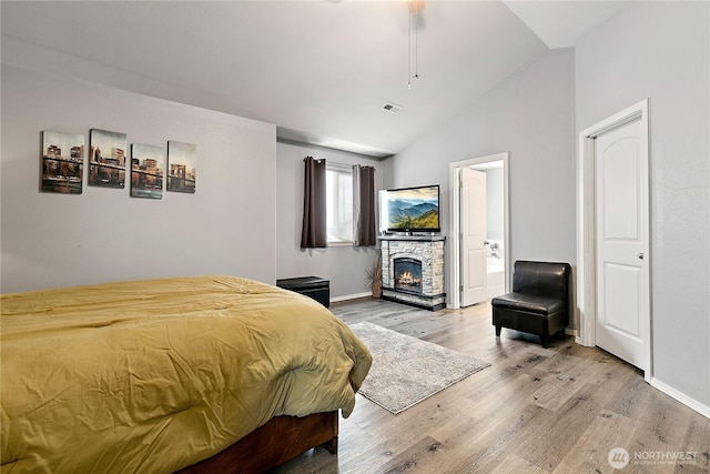 bedroom with light wood-type flooring, vaulted ceiling, a stone fireplace, and baseboards