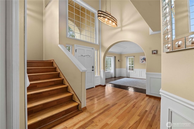 entryway with crown molding, stairway, wainscoting, wood finished floors, and arched walkways