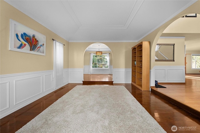 empty room with a wealth of natural light, dark wood-style floors, arched walkways, and a tray ceiling