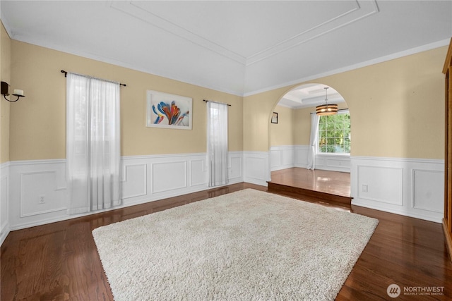 empty room featuring a wainscoted wall, dark wood-type flooring, arched walkways, and a tray ceiling