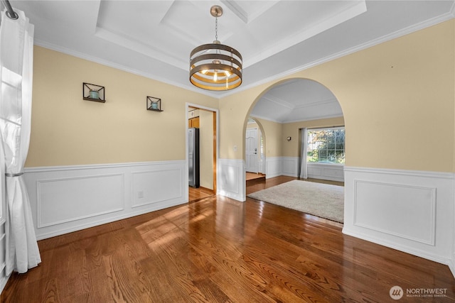 unfurnished dining area featuring wood finished floors, arched walkways, wainscoting, a raised ceiling, and a chandelier