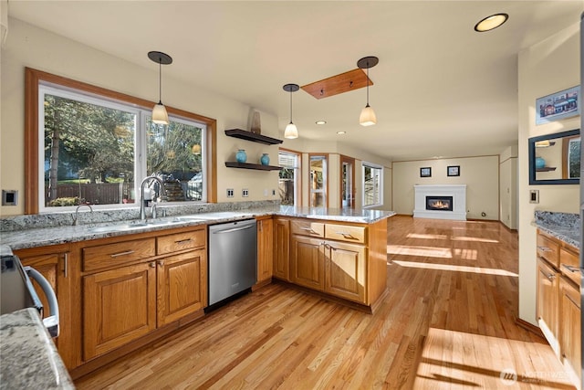 kitchen featuring a glass covered fireplace, light stone countertops, light wood-style flooring, a sink, and dishwasher