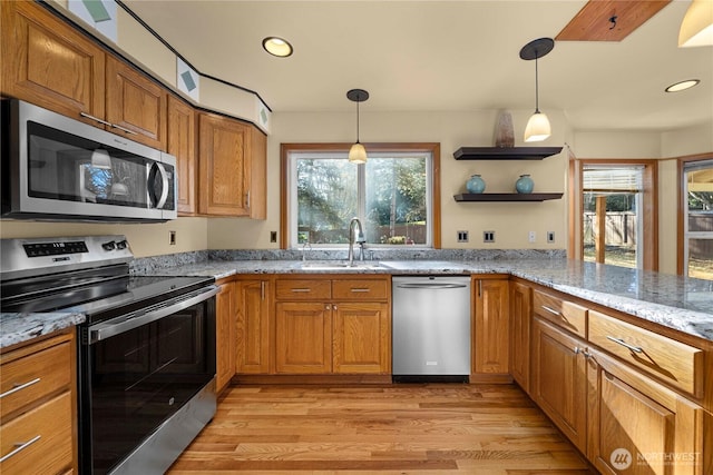 kitchen with light stone counters, brown cabinetry, a sink, stainless steel appliances, and light wood-style floors