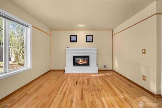 unfurnished living room with light wood finished floors, plenty of natural light, a brick fireplace, and visible vents