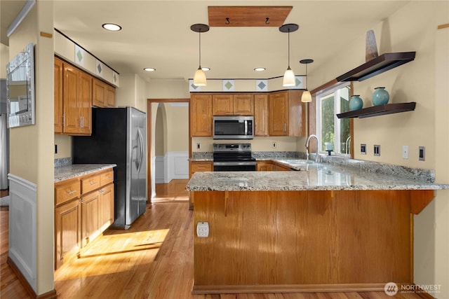 kitchen featuring light stone counters, appliances with stainless steel finishes, a peninsula, brown cabinetry, and a sink