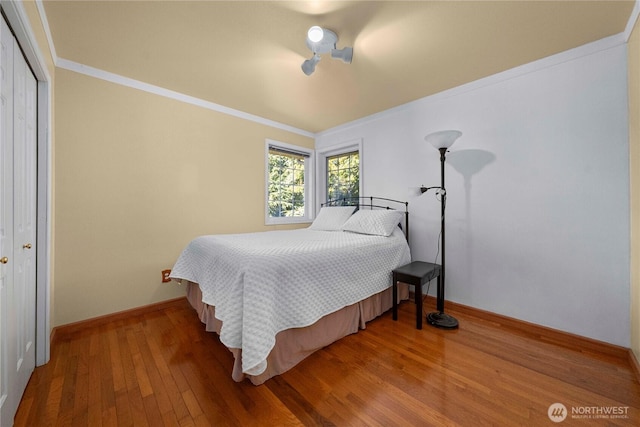 bedroom with a closet, crown molding, baseboards, and wood-type flooring