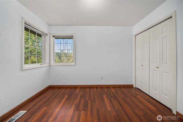 unfurnished bedroom with dark wood-type flooring, baseboards, visible vents, and a closet