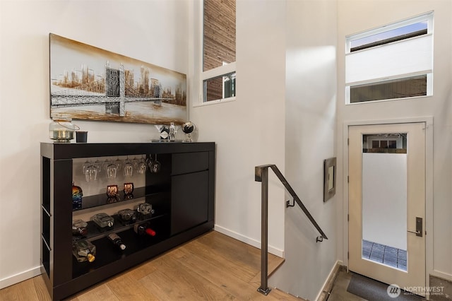 bar with baseboards, a bar, and light wood-style floors