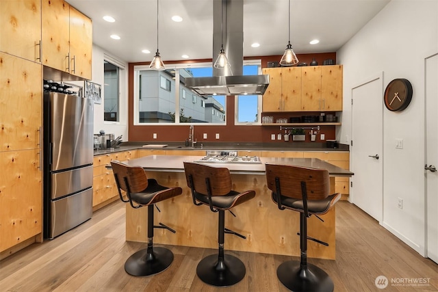 kitchen with a sink, hanging light fixtures, freestanding refrigerator, light brown cabinetry, and island exhaust hood