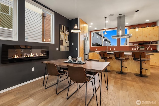 dining space with light wood-style floors, recessed lighting, baseboards, and a glass covered fireplace