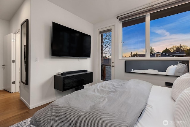 bedroom with baseboards, wood finished floors, and access to exterior