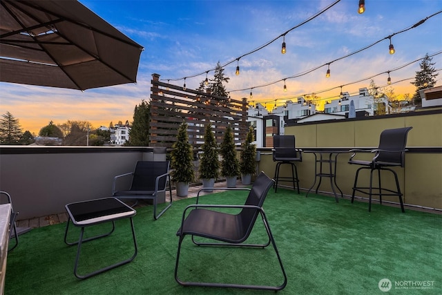 patio terrace at dusk featuring an outdoor bar and a lawn