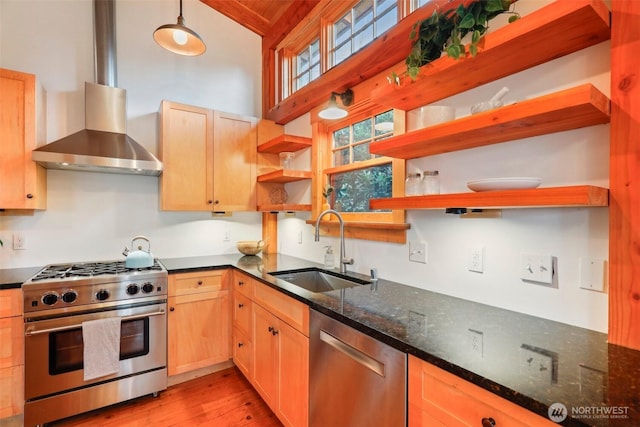 kitchen with stainless steel appliances, a sink, wall chimney range hood, dark stone counters, and open shelves