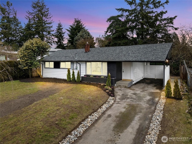 ranch-style house with a shingled roof, a lawn, concrete driveway, a chimney, and fence