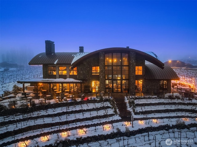 snow covered property with a standing seam roof, metal roof, and a chimney