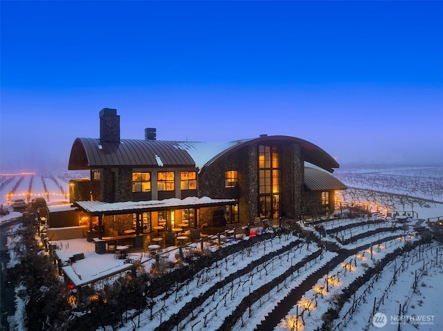 snow covered rear of property with a standing seam roof, metal roof, and a chimney