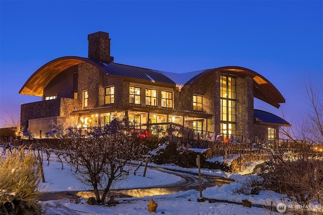 snow covered back of property featuring metal roof, a standing seam roof, and a chimney