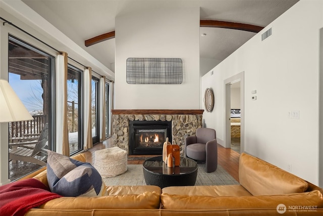 living area featuring light wood-style floors, visible vents, a fireplace, and lofted ceiling with beams