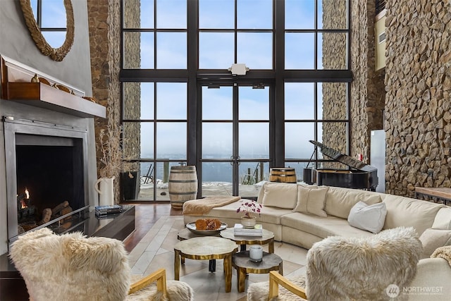 living room featuring a wall of windows, a warm lit fireplace, a water view, and a high ceiling