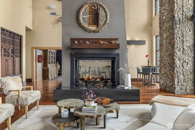 living area with light wood-type flooring, a multi sided fireplace, a towering ceiling, and baseboards