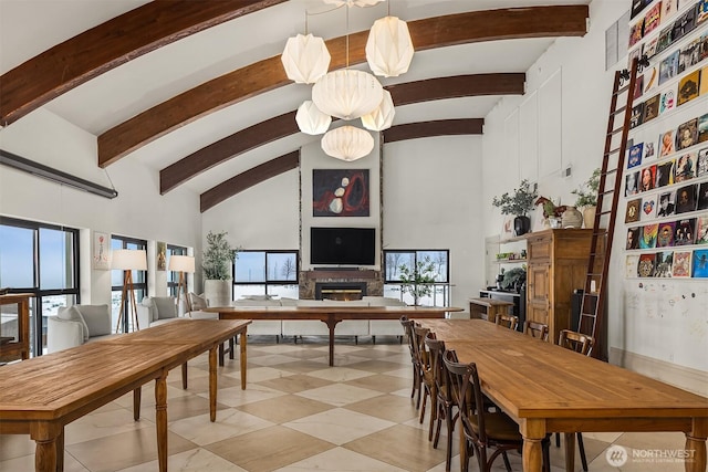 dining area featuring a glass covered fireplace, beam ceiling, plenty of natural light, and a high ceiling