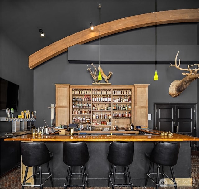 bar featuring brick floor, indoor wet bar, and vaulted ceiling with beams