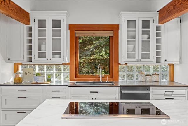 kitchen with a sink, black electric stovetop, white cabinets, and glass insert cabinets