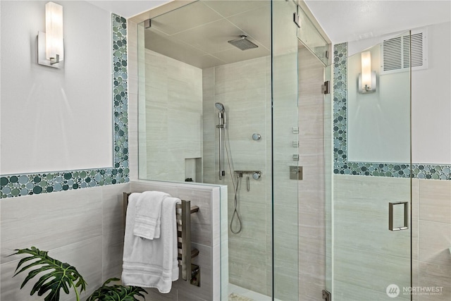 bathroom featuring tile walls, a shower stall, and visible vents