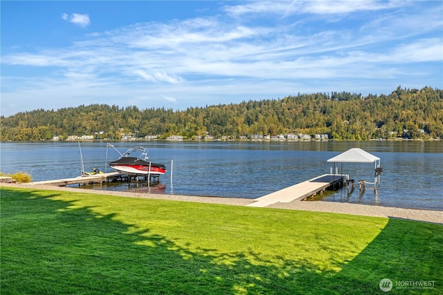 dock area with a yard, boat lift, a water view, and a wooded view