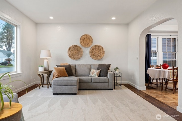 living room featuring arched walkways, recessed lighting, baseboards, and wood finished floors