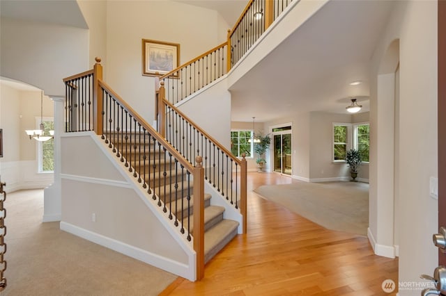 stairway featuring arched walkways, a high ceiling, an inviting chandelier, and wood finished floors