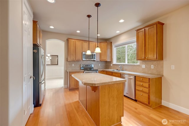 kitchen with a sink, light countertops, appliances with stainless steel finishes, backsplash, and a center island