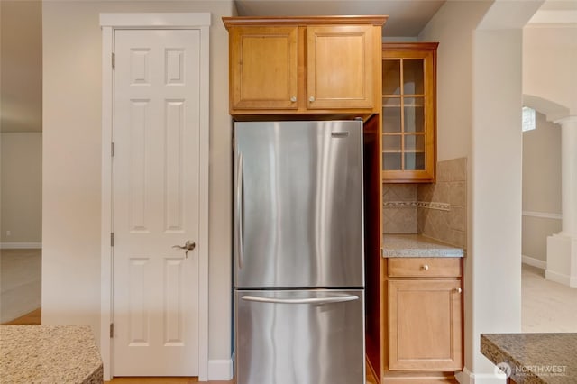 kitchen with tasteful backsplash, glass insert cabinets, baseboards, freestanding refrigerator, and ornate columns