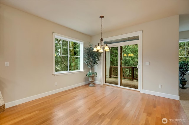 spare room with baseboards, light wood-type flooring, and a chandelier