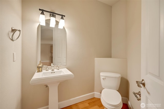 half bathroom with toilet, baseboards, and wood finished floors