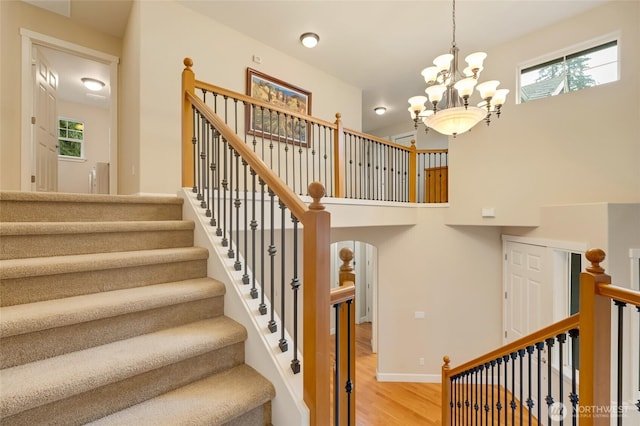 stairway featuring a chandelier, a towering ceiling, baseboards, and wood finished floors