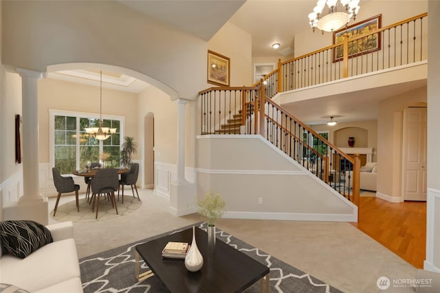 living area featuring stairway, decorative columns, arched walkways, a towering ceiling, and a chandelier