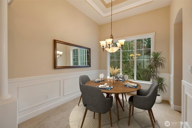 dining room featuring light colored carpet, arched walkways, a notable chandelier, and wainscoting