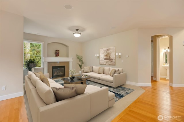 living room with baseboards, arched walkways, light wood-style floors, and a glass covered fireplace