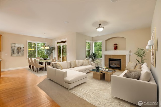 living room with a chandelier, a glass covered fireplace, plenty of natural light, and light wood-type flooring