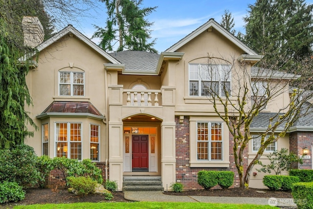 view of front of house featuring a balcony, stucco siding, roof with shingles, and brick siding