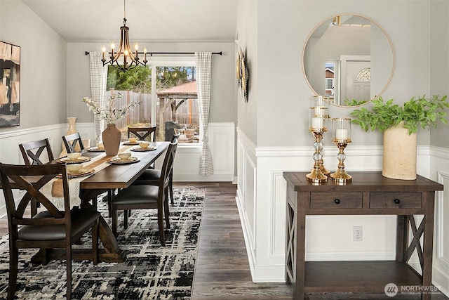 dining space with a wainscoted wall, dark wood-style floors, a decorative wall, and a notable chandelier