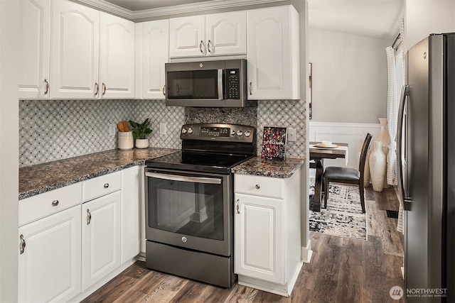 kitchen with a wainscoted wall, stainless steel appliances, white cabinets, backsplash, and dark wood finished floors