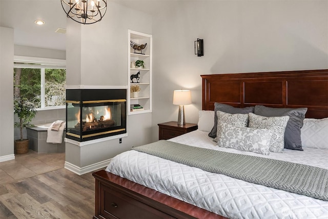 bedroom with visible vents, baseboards, wood finished floors, a notable chandelier, and a multi sided fireplace