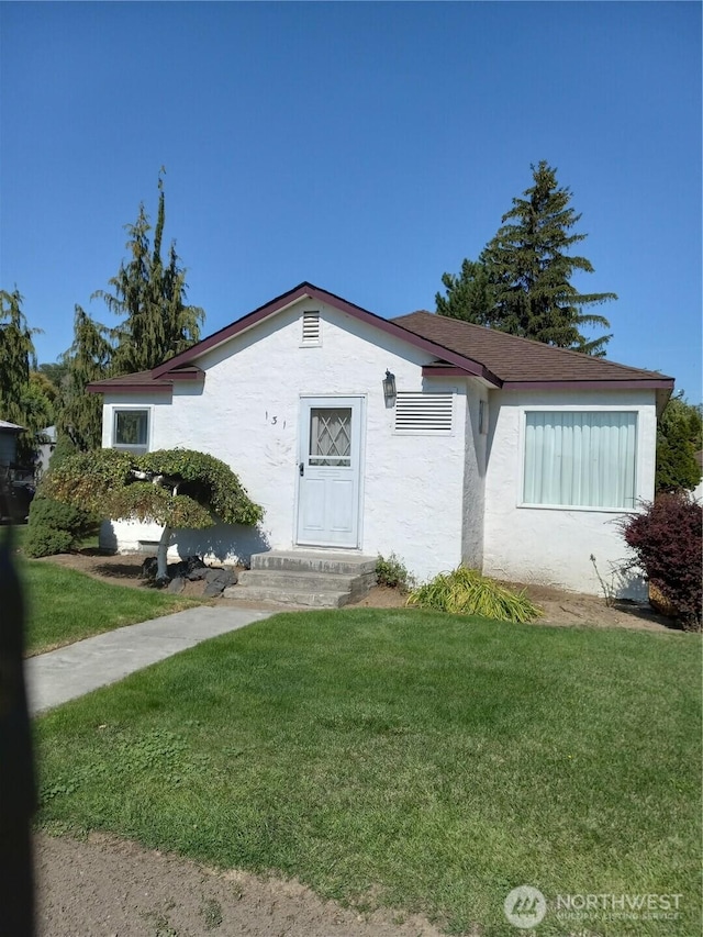 view of front of property with a shingled roof, a front lawn, and stucco siding