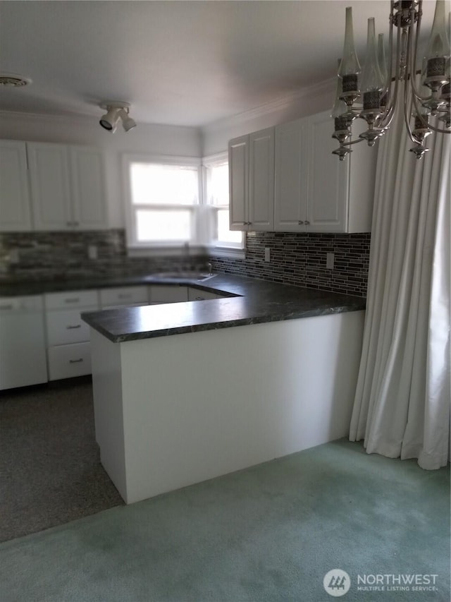 kitchen with white cabinets, dark countertops, backsplash, a sink, and a notable chandelier