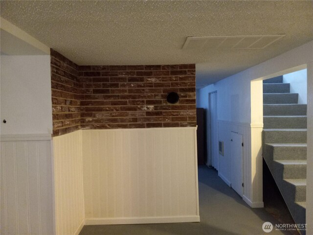 hall with a wainscoted wall, stairway, a textured ceiling, and visible vents