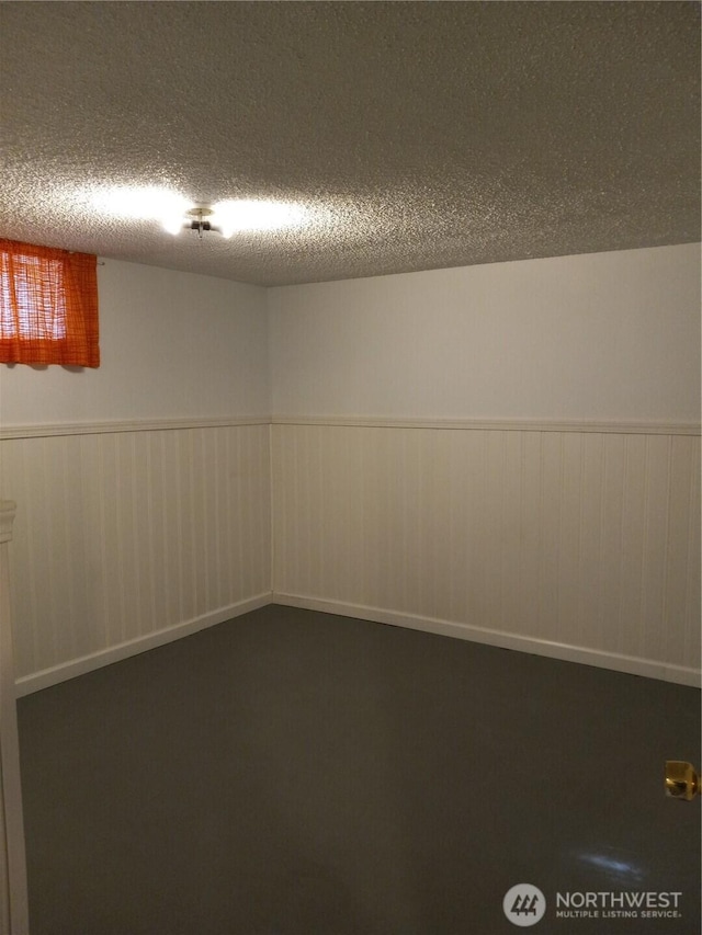 finished basement featuring a textured ceiling and wainscoting